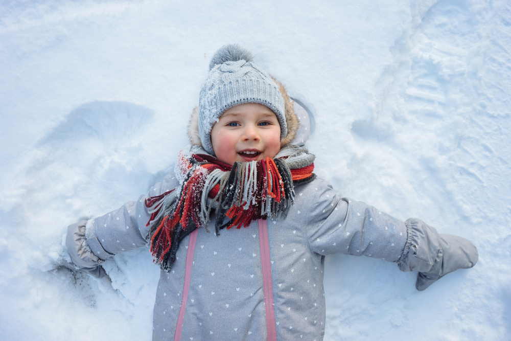 A happy toddler lying in the snow.